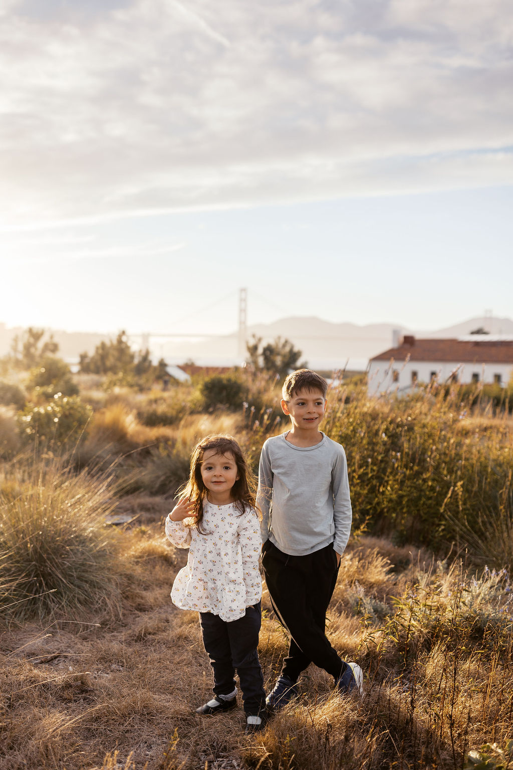 Brother and sister standing in tall grass with the Golden Gate Bridge far behind them