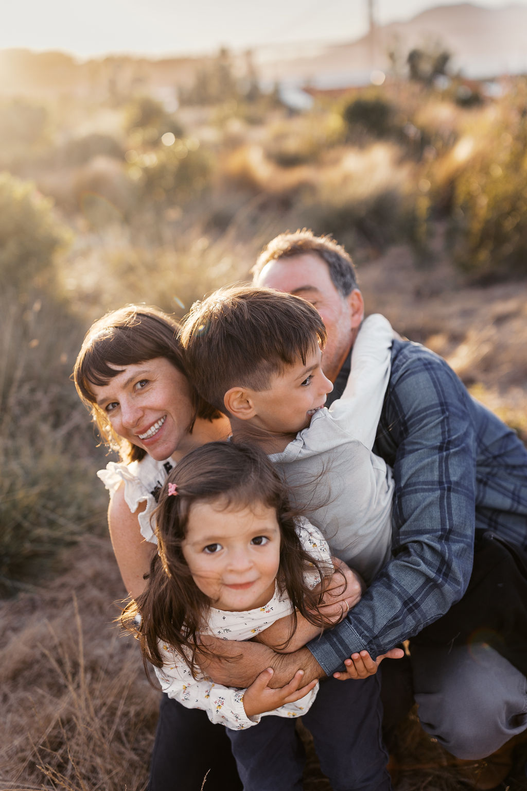 Family of four piled together in golden grass, all laughing, in warm evening light in the Presidio