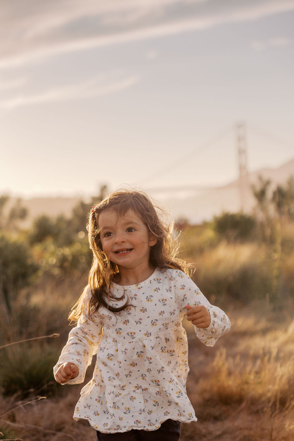 Little girl running through golden grass with the Golden Gate Bridge behind her