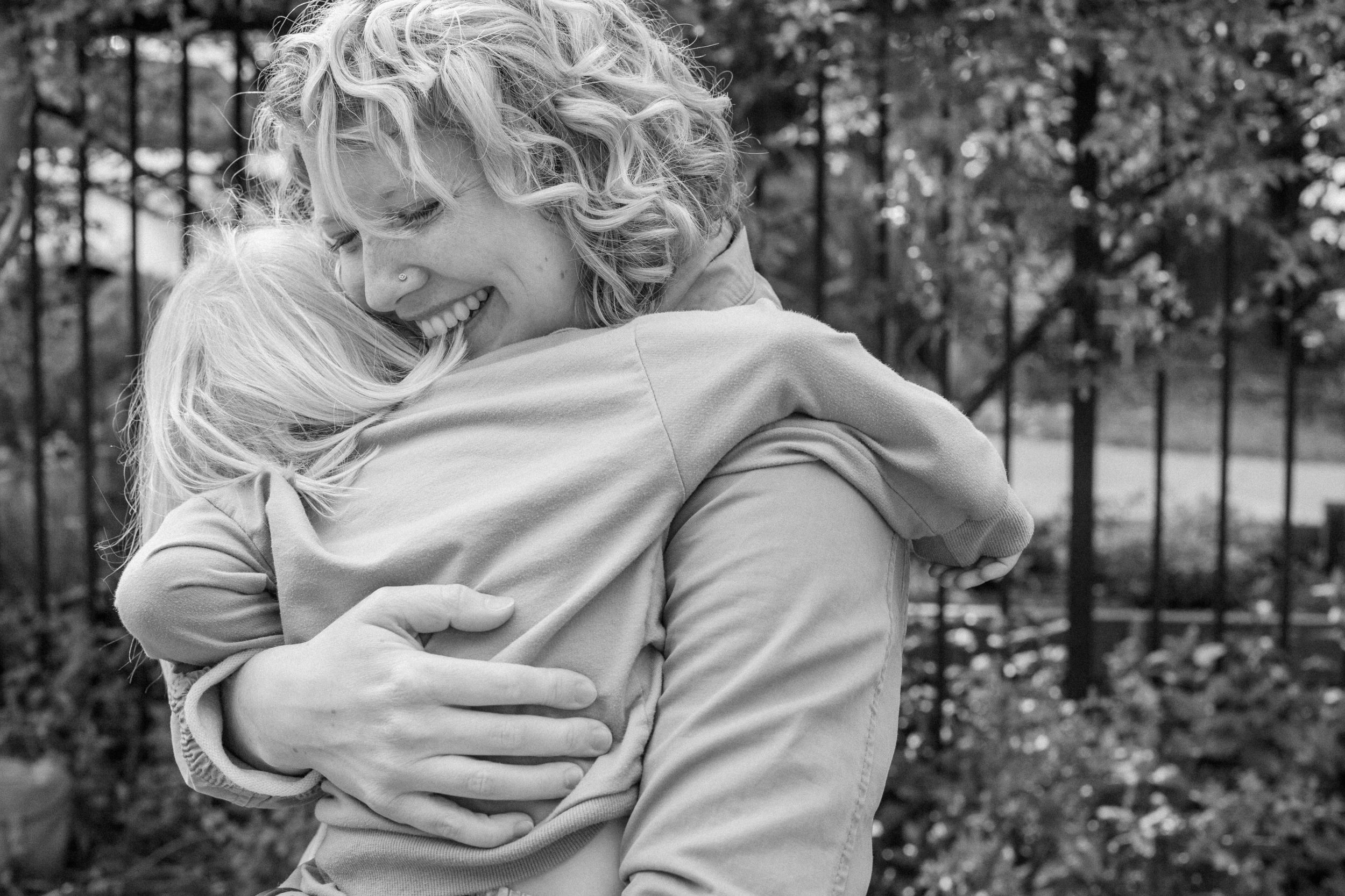 Black and white photograph of a mother embracing her laughing child outdoors