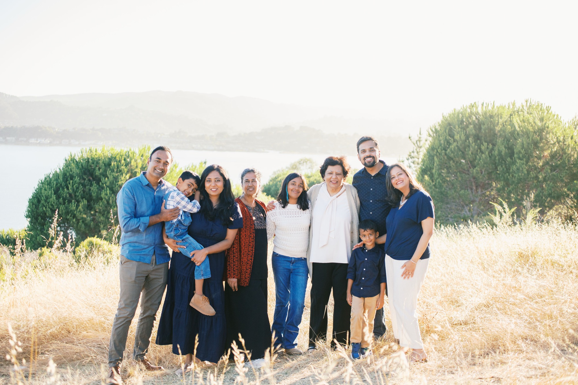 Three generations of one family, nine people strong, standing together in golden grass on the Tiburon hillside with Richardson Bay and the Marin hills behind them