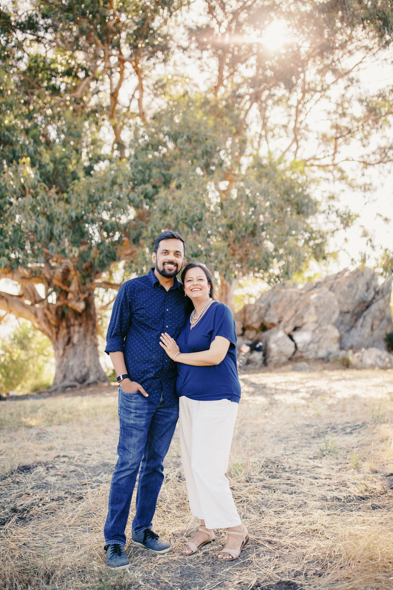 Couple smiling together in front of the Hippie Tree and rocks, backlit by evening sun