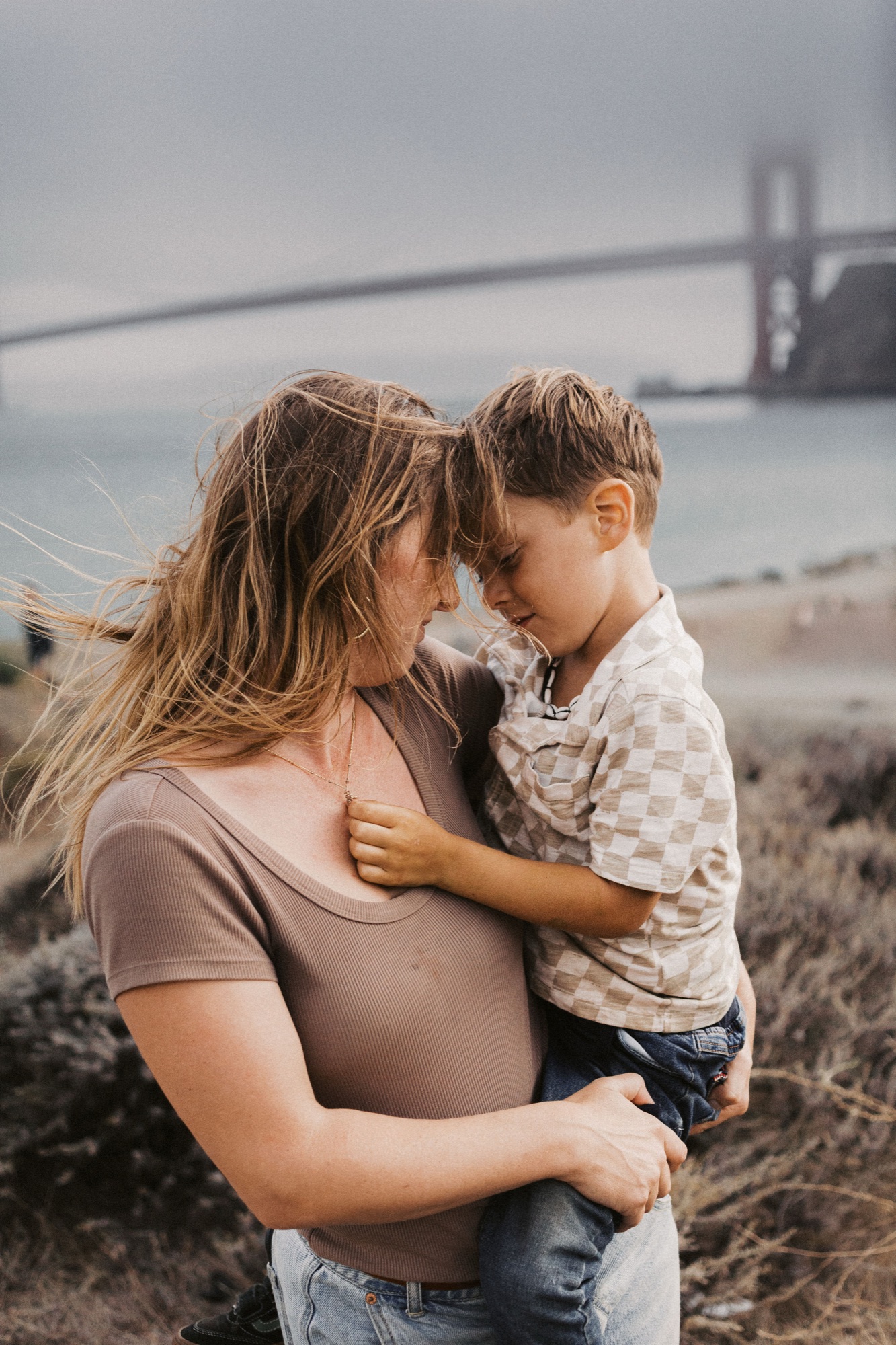 Mom holds her little boy forehead to forehead on the Sausalito bluff, the Golden Gate Bridge in the fog behind them