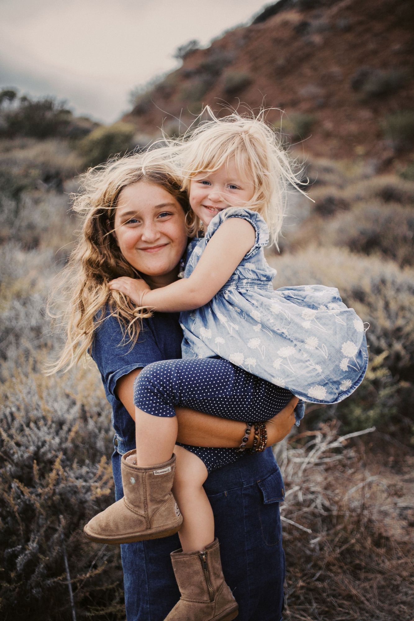 Big sister carries her little sister on the coastal hillside above the bay in Sausalito