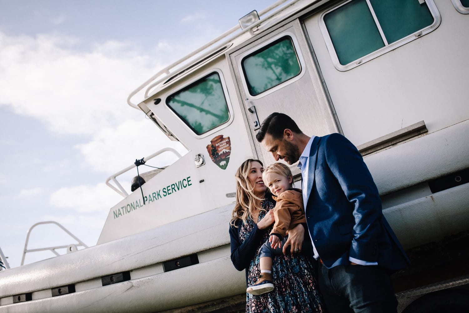 Mom and dad hold their toddler beside a white National Park Service boat, San Francisco family photography