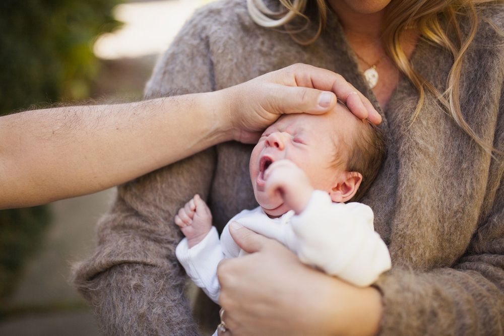 Parent gently holding a yawning newborn outdoors in warm golden light