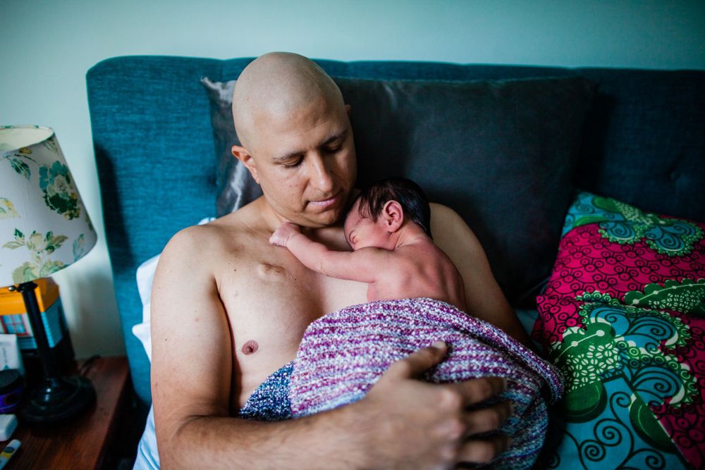 Father holding newborn skin-to-skin on a sofa at home