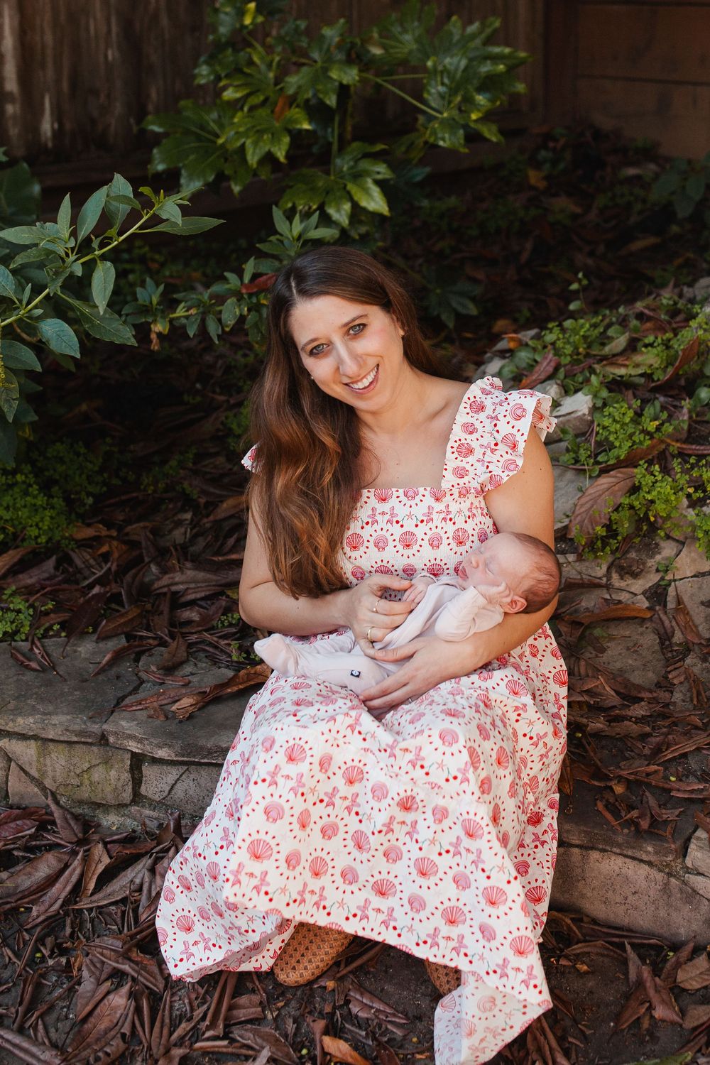 Mother smiling in a garden holding her sleeping newborn