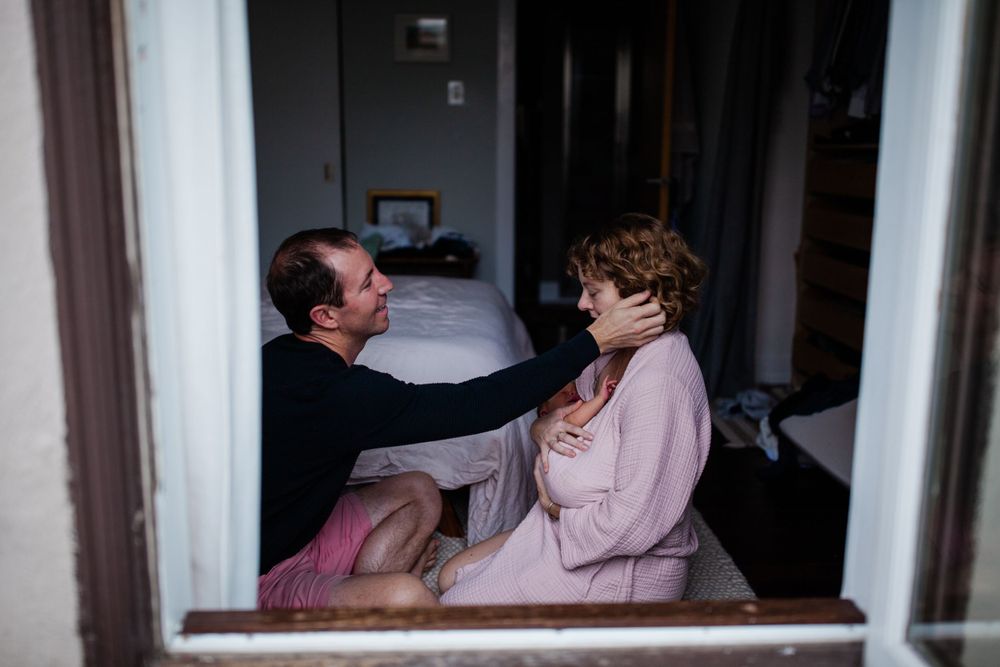 Couple with newborn photographed through a window frame — lifestyle newborn photography in Marin County