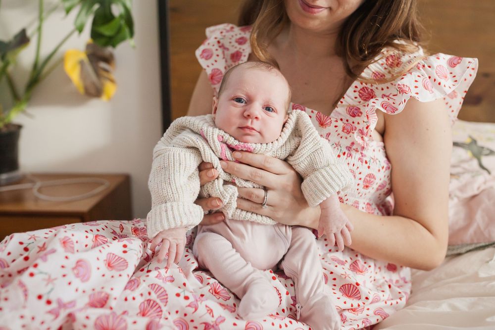Mother in floral dress holds newborn in knit sweater
