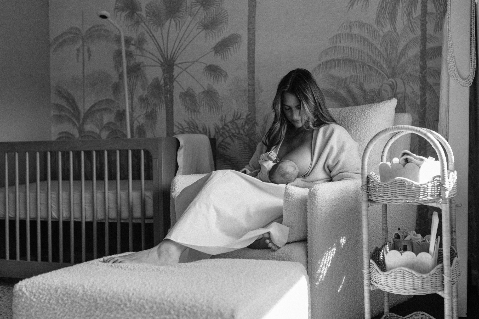 A quiet moment of stillness in her Marin nursery — soft window light washing over her as she nurses her newborn in the boucle chair, the tropical wallpaper and warm shadows making it feel like the rest of the world simply paused. This is exactly the kind of real, unhurried moment that makes lifestyle newborn photography so worth it.