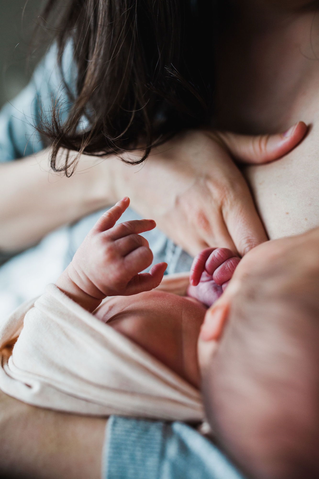 A newborn's tiny hand grasps an older sibling's finger while resting against their chest in soft natural light
