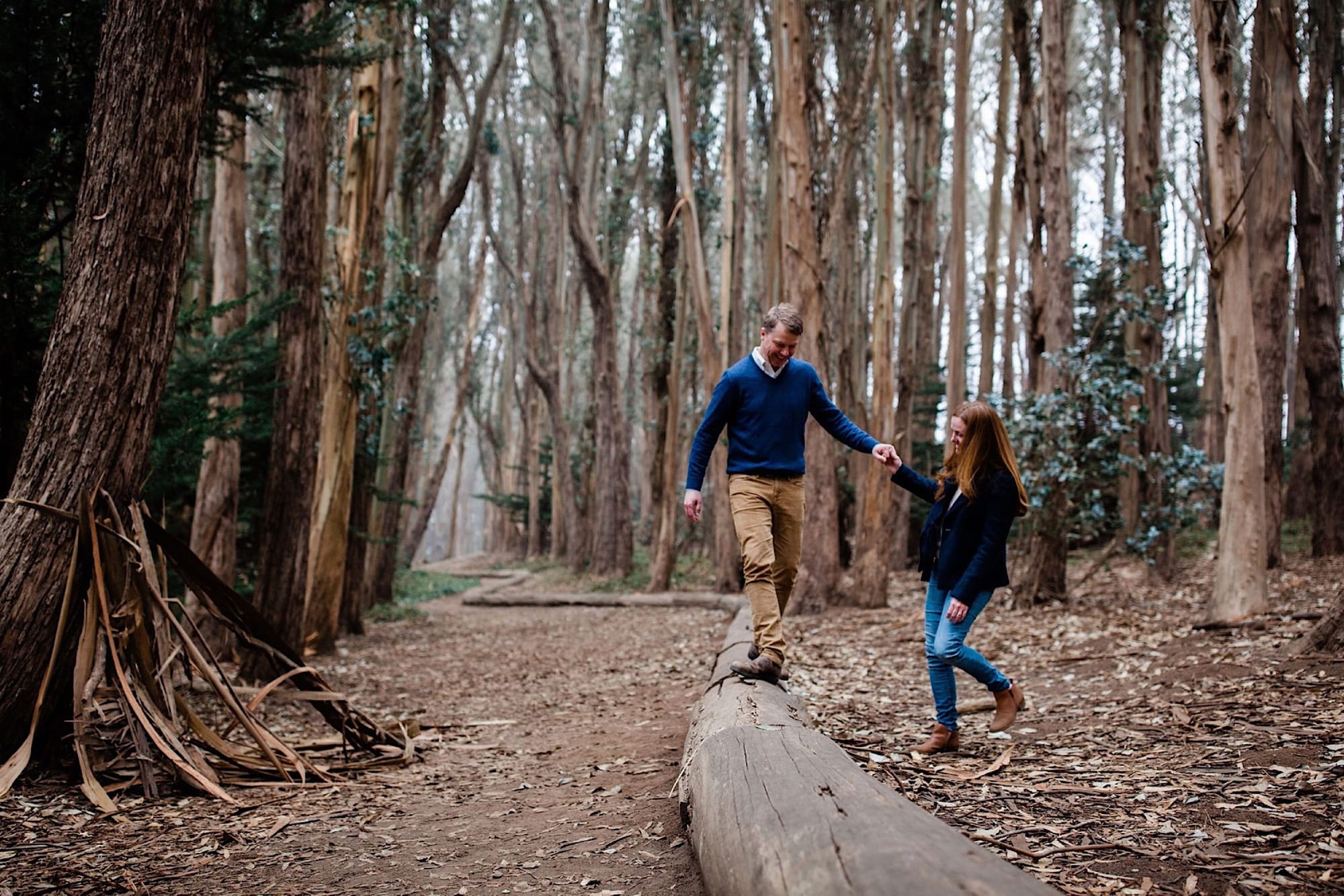 Couple walking a fallen log hand in hand with the eucalyptus lane stretching behind them