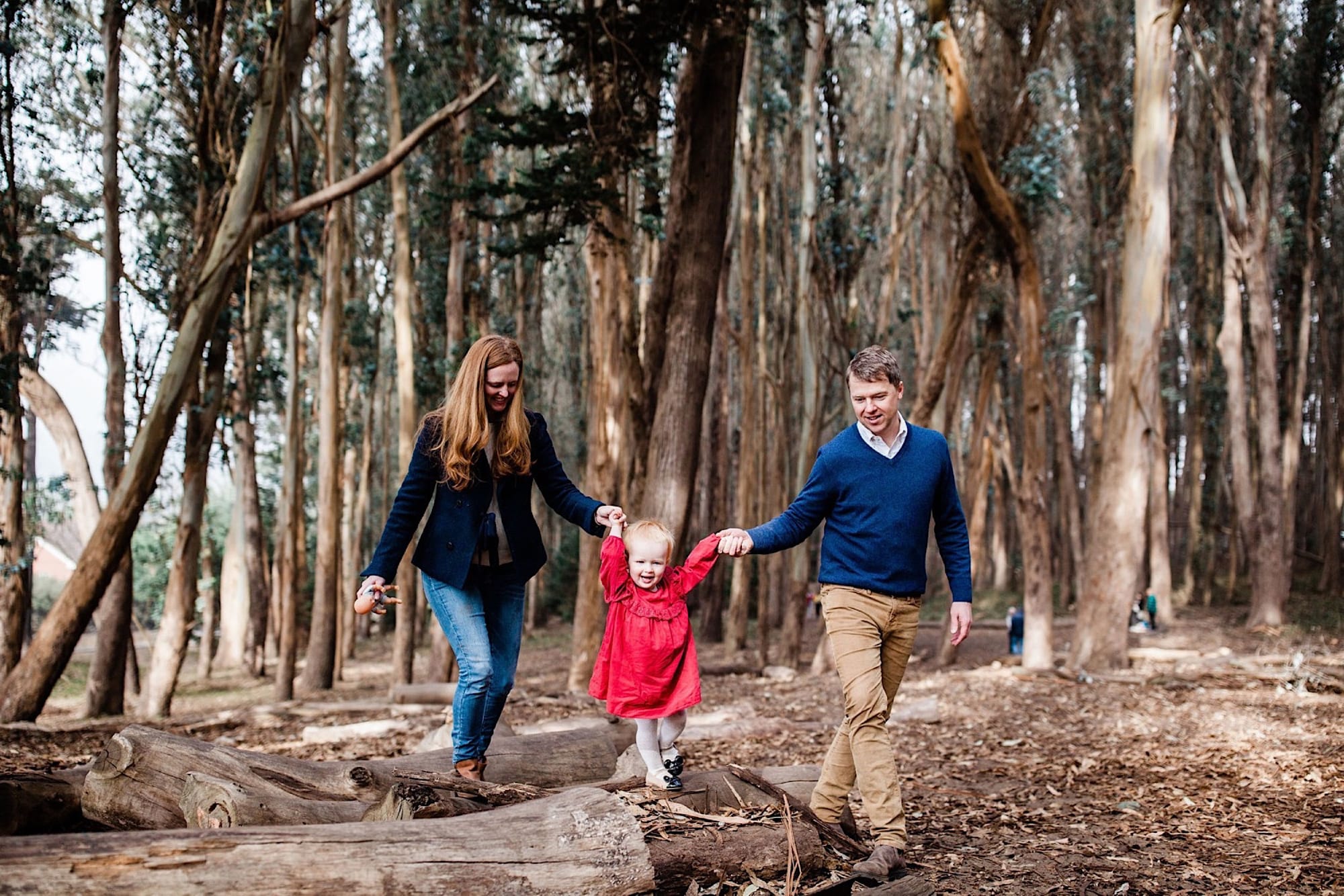 Mom and dad walking their little girl along a fallen log on Lovers Lane in the Presidio
